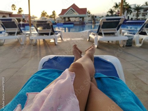 Girl's feet on a sun lounger against the backdrop of the pool