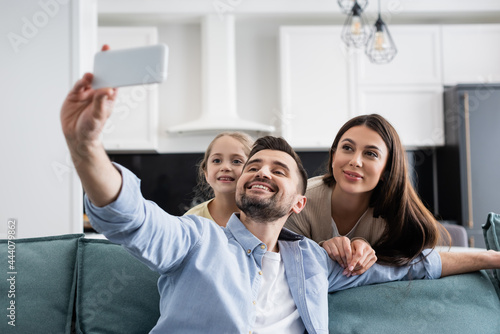 cheerful man taking selfie on mobile phone with smiling family at home