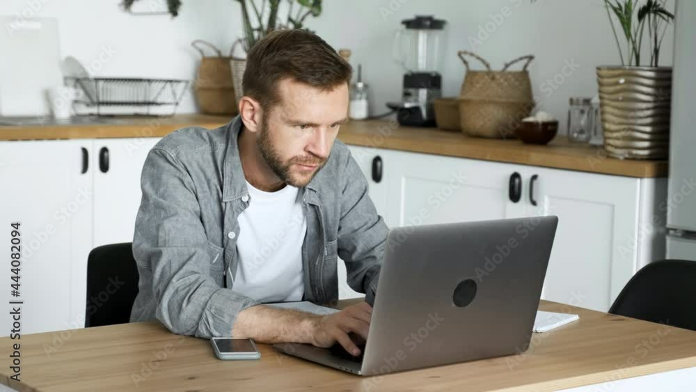 A Young Freelance Man Works At A Computer, Looks at The Monitor Screen, Is in A Room At Home A Young Freelance Man Works At A Computer, Looks at The Monitor Screen, Is in A Room At Home