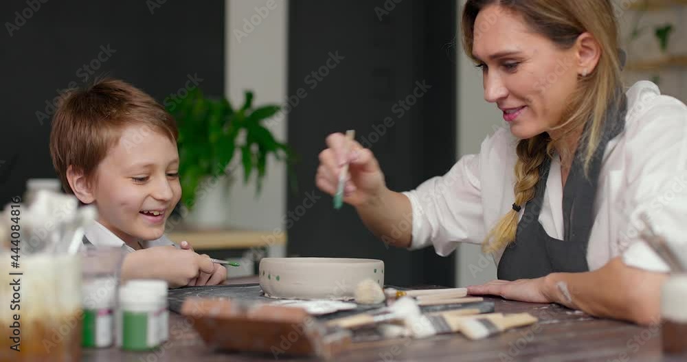 Mother potter helping his son making pattern on the bowl in pottery studio. Master class in a pottery workshop. Mother potter helping his son making pattern on the bowl in pottery studio. Master class in a pottery workshop.