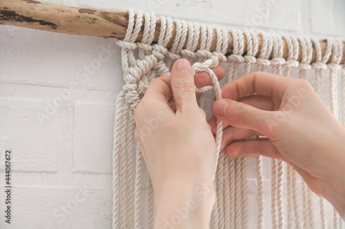 woman knits weaving macrame pinned on a wooden stick