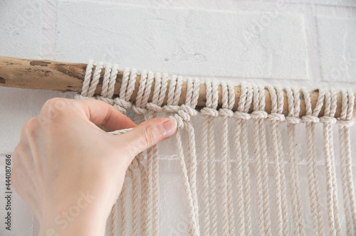 woman knits weaving macrame pinned on a wooden stick