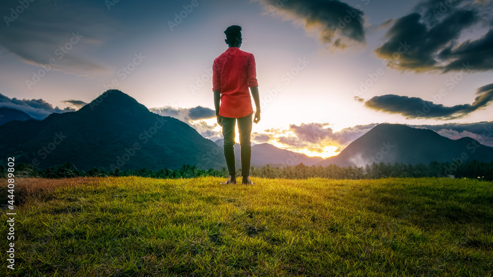 An adult standing on a mountain against beautiful sunset background. 
