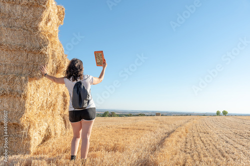 middle-aged brunette latina woman standing consulting a tablet leaning against a pile of straw bales