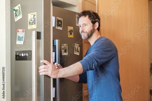 Adult man opening fridge in his kitchen