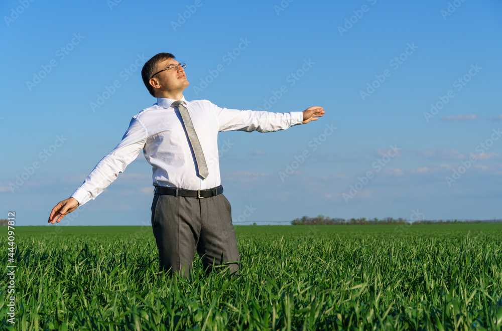 businessman poses in a field, he looks into the distance and rests, green grass and blue sky as background businessman poses in a field, he looks into the distance and rests, green grass and blue sky as background