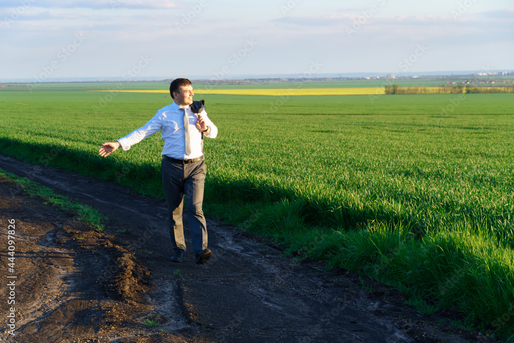 businessman walks along a country road, green field, freelance and business concept, green grass and blue sky as background businessman walks along a country road, green field, freelance and business concept, green grass and blue sky as background