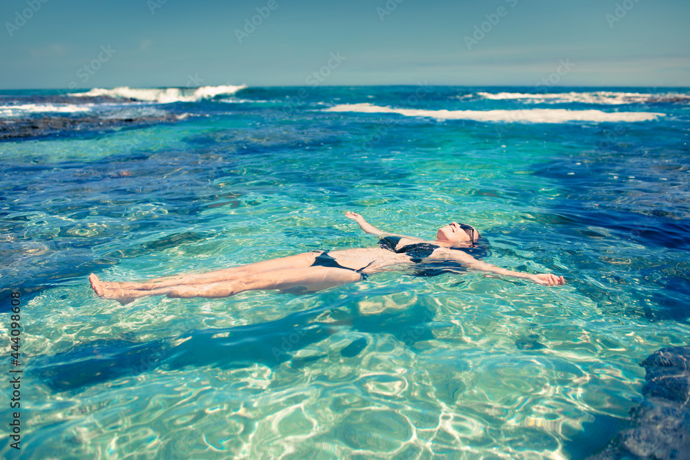 Female lying swimming in crystal clear turquoise water on a beach in Hawaii. tropical beach holiday vacation. 