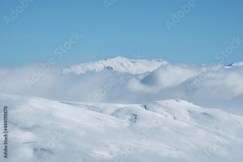 Snow covered mountain slope with clouds and bright blue sky. Winter mountain landscape