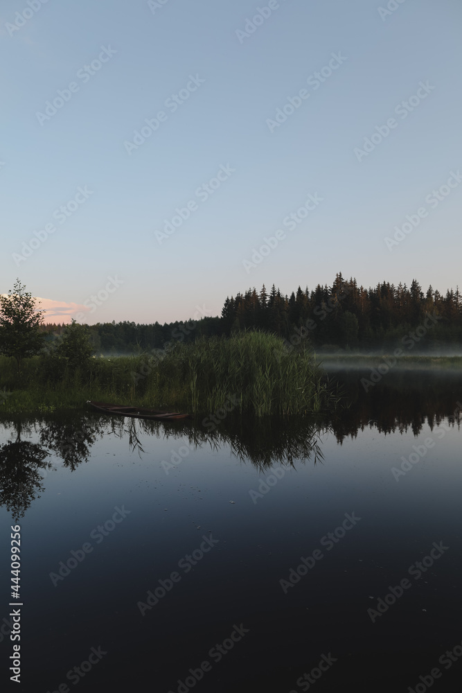 summer evening twilight view on picturesque plain lake surface with reflections of sky and trees