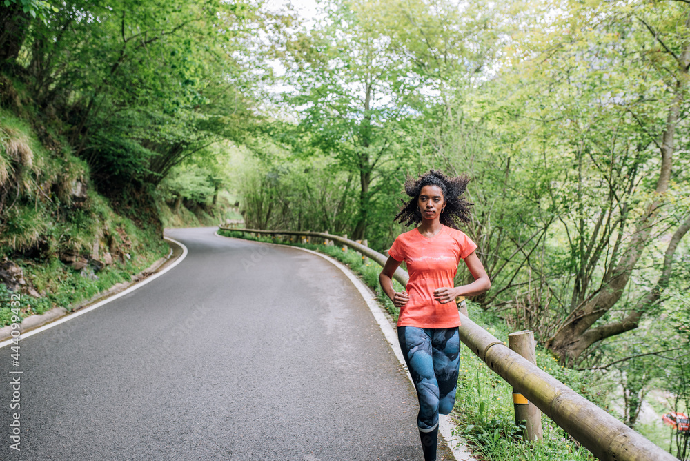 Sportswoman running on empty paved road in woods Sportswoman running on empty paved road in woods