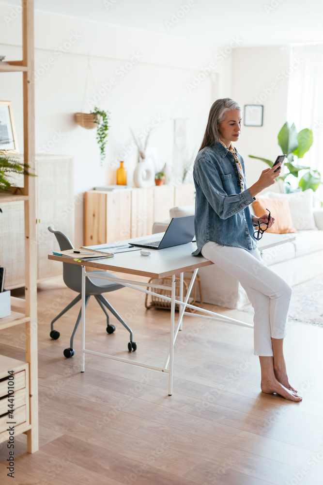 Mature female leaning on desk and browsing cellphone Mature female leaning on desk and browsing cellphone
