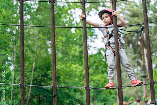 Little girl in a protective helmet, an insurer walks your way in a rope park. The child holds wooden pillars © speed300