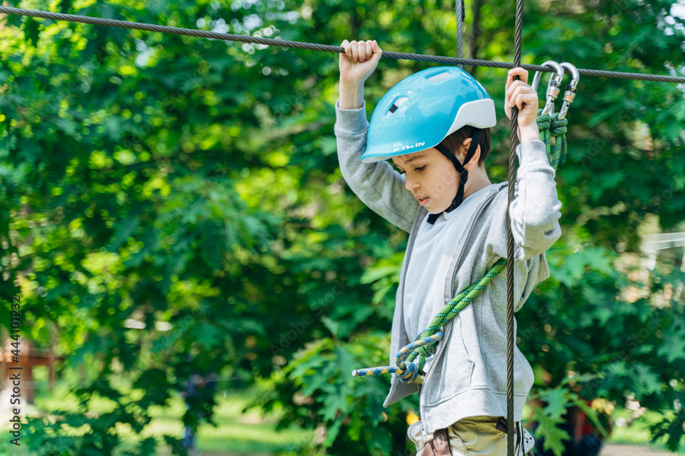 Concentrated boy holding a rope, walking along the rope. A child in a rope park Concentrated boy holding a rope, walking along the rope. A child in a rope park