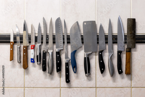 Many different knives are attached to a magnetic knife holder on the wall. photo