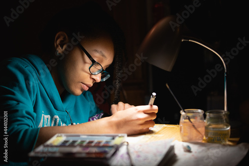 Teenager working on art for school by lamplight photo