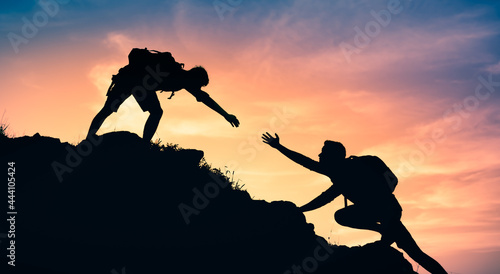 Team work, life goals and self improvement concept. Man helping his female climbing partner up a steep edge of a mountain.