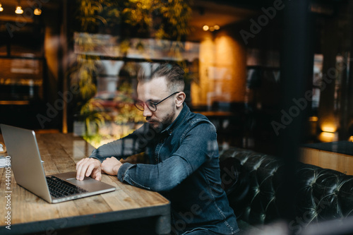 young man working in coworking cafe with laptop, online business remote work in quarantine.