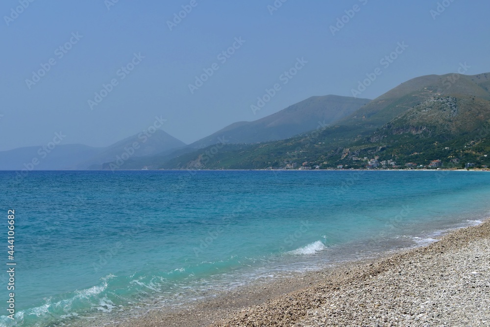 Clean beach and crystal sea in different shades of blue on blurred background of mountains Clean beach and crystal sea in different shades of blue on blurred background of mountains