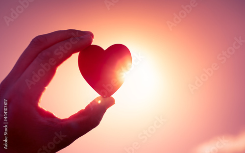 Hand holding heart on beautiful sky background. 