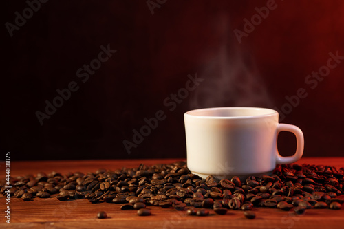 Warm cup of coffee and coffee beans on dark background. Coffee cup and coffee beans on wooden table