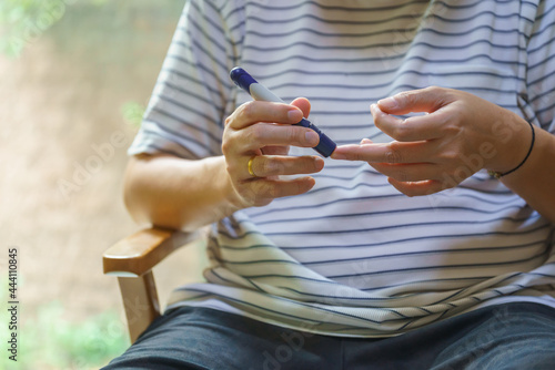 Close up of man hands using lancet on finger to check blood sugar level by Glucose meter. Use as Medicine, diabetes, glycemia, health care and people concept.