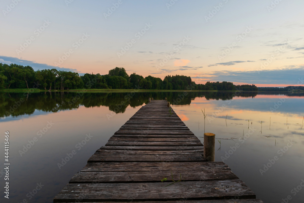 Obraz premium View of the lake with a wooden footbridge in the center of the photo. Outdoor summer evening