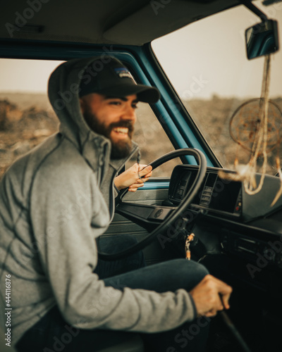 Caucasian boy driving a vintage van around Lanzarote island in February with volcanic landscape and dream catcher as decoration while the sun hides on the horizon photo