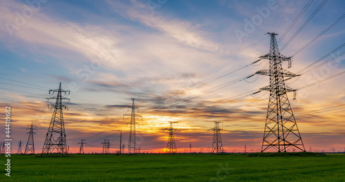 Schilderij op canvas high voltage lines and power pylons in a green agricultural field against a satu