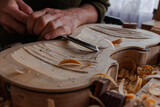 Luthier's hands using gouge to work the wood and make a violin