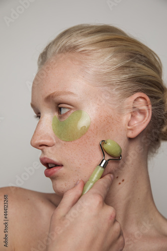 Model with green jade roller and under-eye patch photo