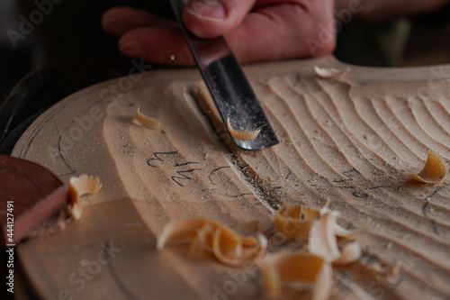 Luthier's hands using gouge to work the wood and make a violin