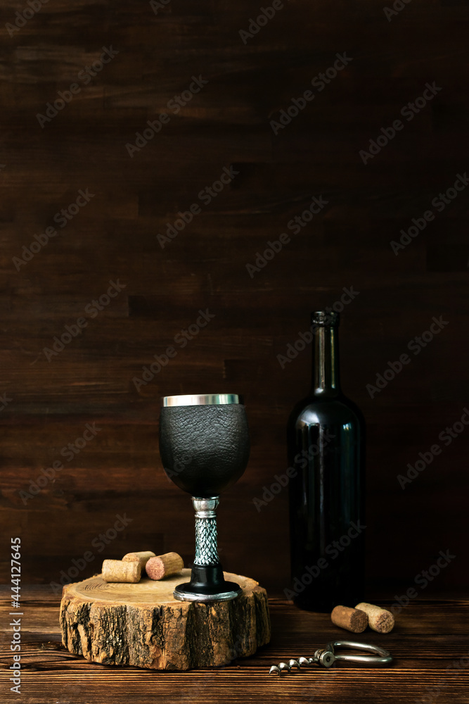 Bottle of red wine and black glass, corkscrew and corks on wooden table, dark alcohol beverage drink background, still life