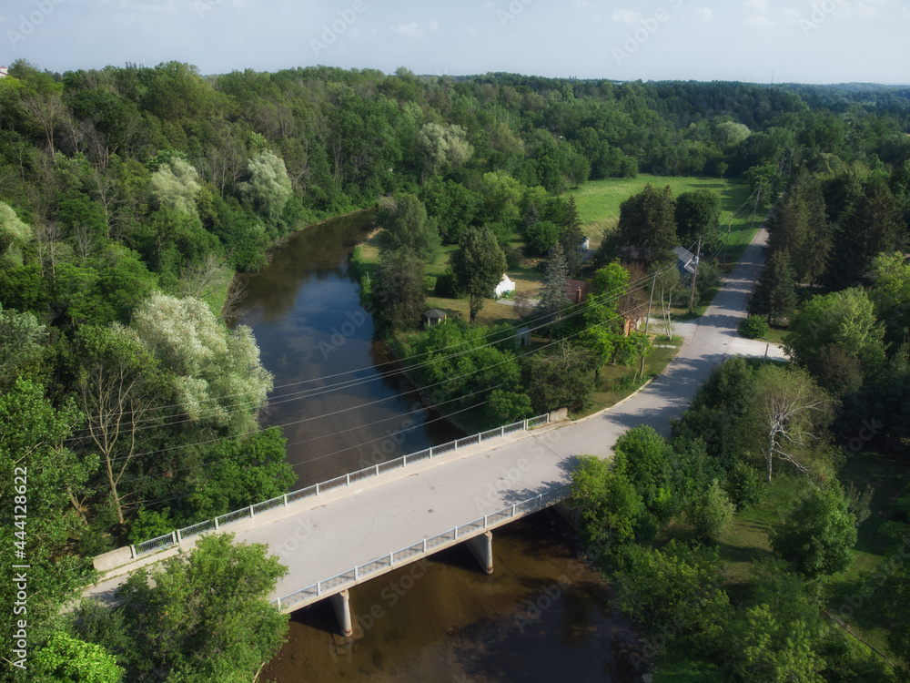 Aerial over the Mill Street bridge over the Credit River in the Cheltenham area, a community within the town of Caledon, Ontario, Canada. Shot by a drone on a hazy summer afternoon.