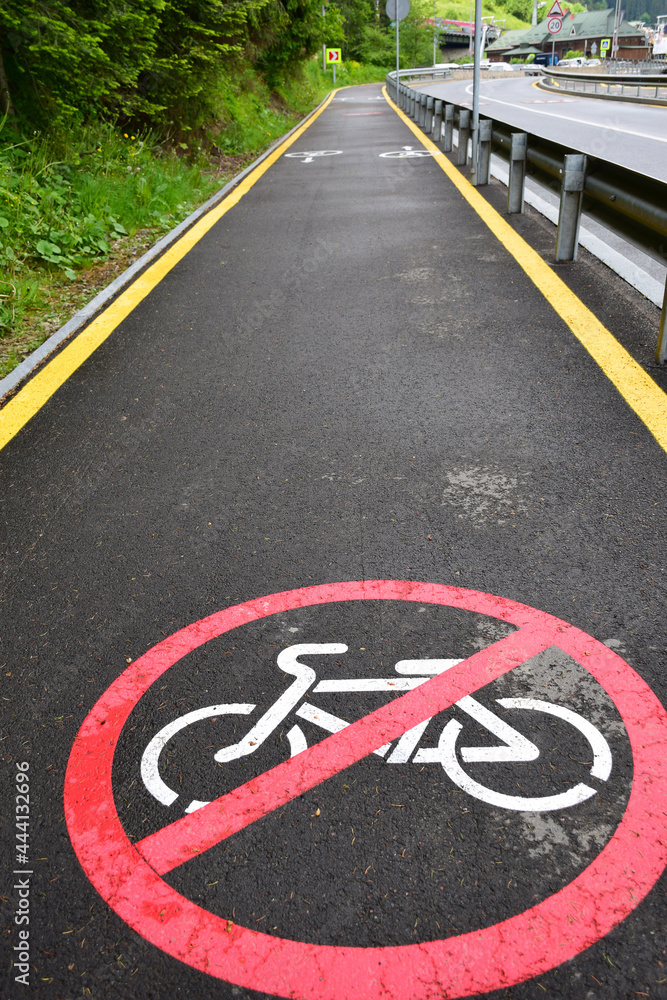 Obraz premium In the foreground, below, on an asphalt footpath, there is a prohibiting cyclist sign. In the background, in perspective, a leaving empty jogging track