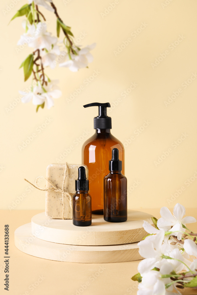 Cosmetics dark amber bottles with natural soap and spring flowers on wooden podium on beige background. Concept natural cosmetics for body care. Cosmetics dark amber bottles with natural soap and spring flowers on wooden podium on beige background. Concept natural cosmetics for body care.