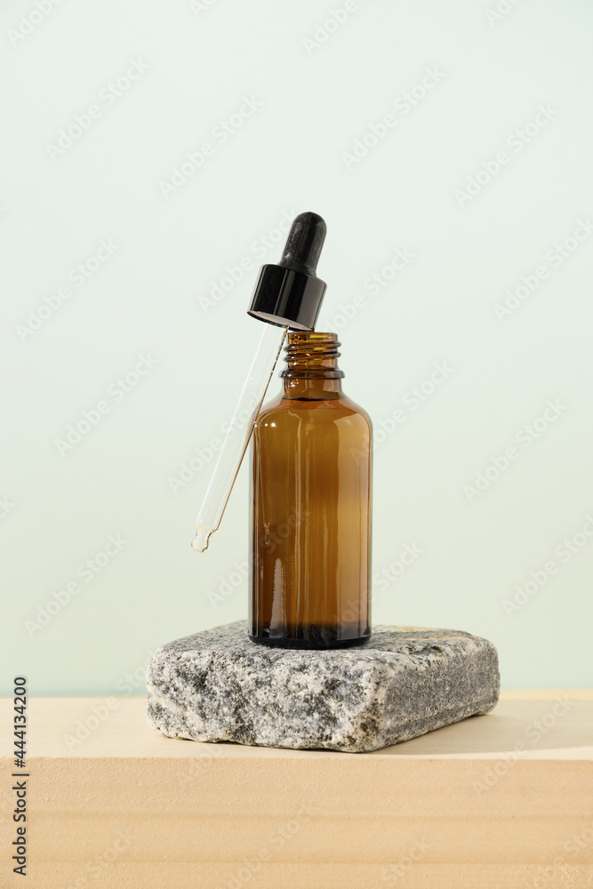 Transparent glass bottle essential oil with dropper on stone on natural beige and blue light background. Vertical format. Close up.