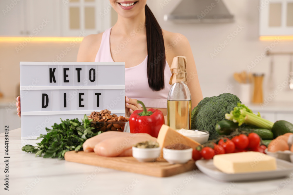 Happy woman near lightbox with words Keto Diet and different products in kitchen, closeup