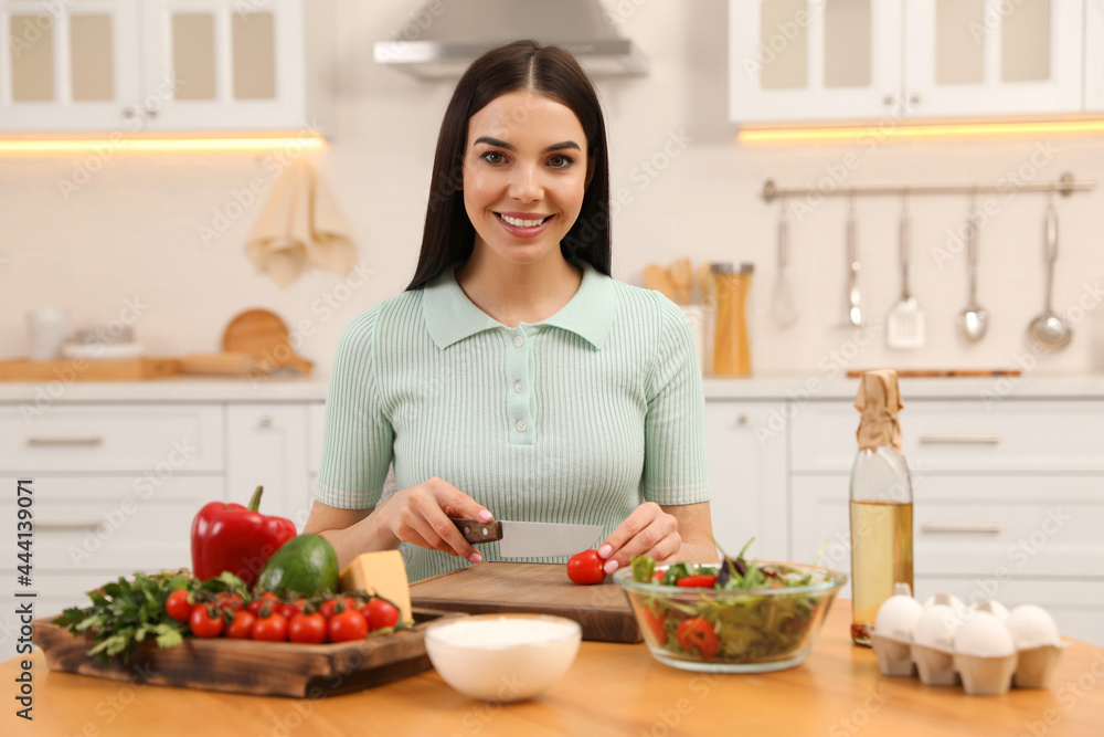 Happy woman cooking salad at table in kitchen. Keto diet