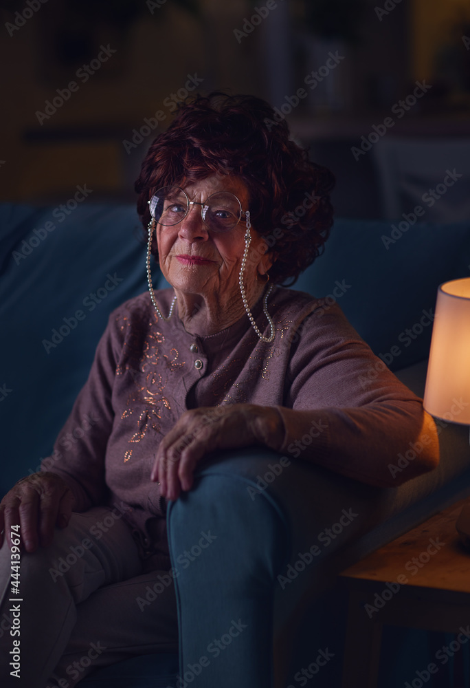 portrait of elegant mature woman sitting on sofa at home and watching tv at night. 84 years old woman