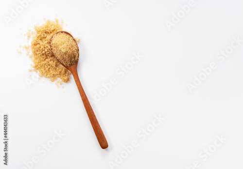 Wooden spoon and brown sugar placed on a white background.