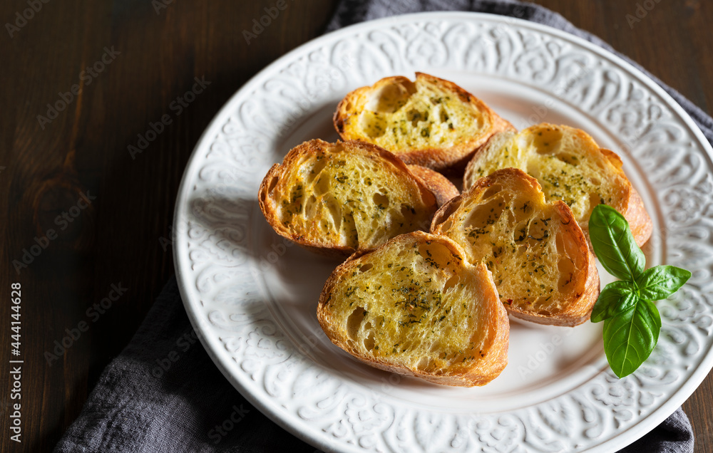 Sliced baked bread with garlic and herbs on a white plate on the table.