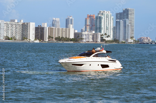 Foto High-end cabin cruiser idling on the Florida Intra-Coastal Waterway with condominium apartment buildings on the Waterway shoreline in the background