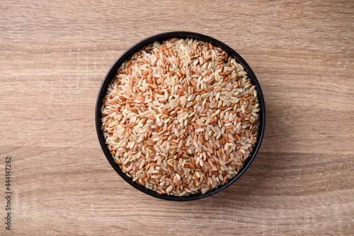 Organic Thai highland brown rice grain in a bowl on wooden background (Cargo rice, Loonzain rice or Husked rice), Healthy food, Table top view photo