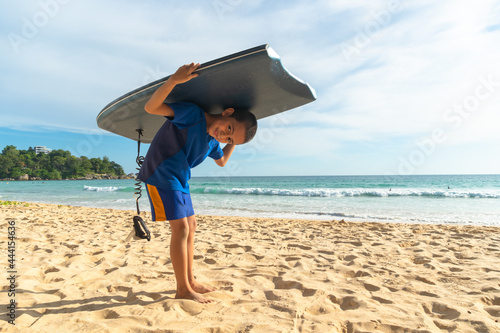 A boy have fun warm up with body board before go to surf..Paradise beach blue sea, and clear sand landscape. .waves crashing on the beach background.