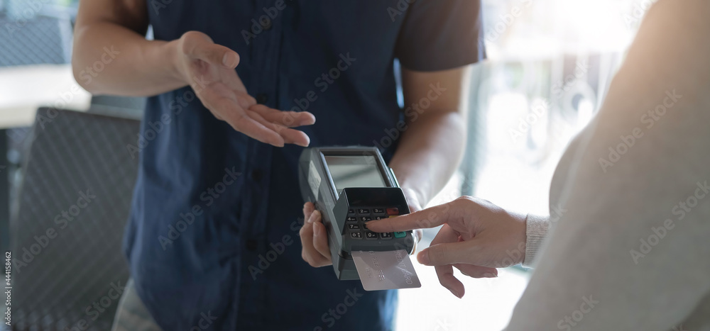 Obraz premium Woman paying by credit card and entering pin code on reader holded in coffee. Customer using credit card for payment. Mature cashier accepting payment over nfc technology.