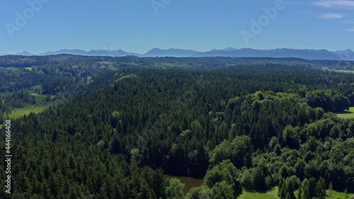 Wide green forest - smooth drone flight backwards in mountain range with a little pond called Moosbach in the foreground - idyllic landscape in southern bavaria, germany. photo