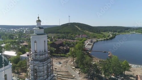 Aerial view of Construction of a embankment in the provincial town with church. Reconstruction of the old church and old houses. Next to the pond is an old factory. Trees and building materials on the photo