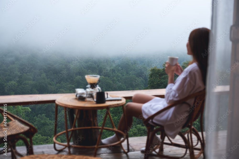 Blurred image of a woman drinking drip coffee and looking at a beautiful nature view on foggy day
