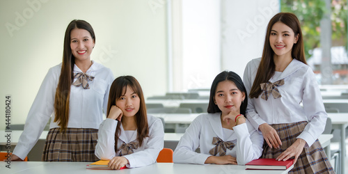 Two young attractive female asian high school students  in white shirt brown checkered school uniform sitting in classroom in school campus. Concept for education © Bangkok Click Studio